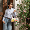 Woman in a strip blouse and blue jeans stylishly posing and showing off her Dreams Blossom Shoulder Bag set in a modern background.
