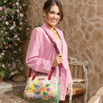 Woman in pink blazer smiling holding our Nicole Lee Dreams Blossom handbag in a modern background.