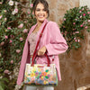 Woman in pink blazer smiling away holding our Nicole Lee  Dreams Blossom Satchel in a modern background.
