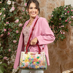 Woman in pink blazer smiling away holding our Nicole Lee  Dreams Blossom Satchel in a modern background.