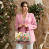 Woman in pink blazer looking away holding our Nicole Dreams Blossom Satchel in a modern background.