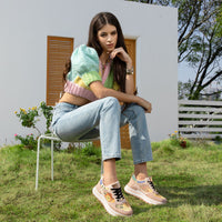WOMEN IN A MULTI COLOR CROP TOP AND BLUE JEANS SITTING IN A BACKYARD WEARING OUR NICOLE LEE FASHION GLITTER SNEAKERS IN NAIL POLISH.