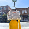 OUR MINI HANDBAG WITH LACER-CUT AND RHINESTONES DETAILS IN COLOR WHITE SET ON A STREET POLE AND BUILDINGS BEHIND.