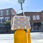 OUR MINI HANDBAG WITH LACER-CUT AND RHINESTONES DETAILS IN COLOR WHITE SET ON A STREET POLE AND BUILDINGS BEHIND.
