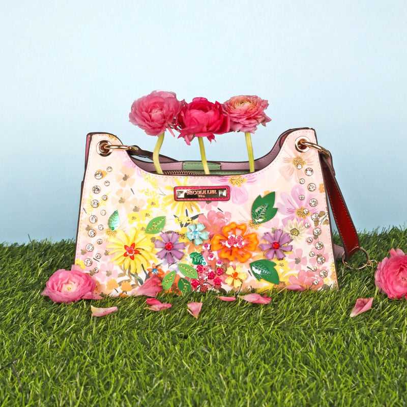 OUR DREAMS BLOSSOM SHOULDER BAG RESTING ON THE GRASS WITH SOME PINK FLOWERS AND PETALS.
