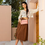 WOMEN IN A IVORY CROCKET CROP TOP AND BROWN SKIRT, HOLDING OUR PINK GRACIE CROSSBODY SET IN A MODERN BACKGROUND. 