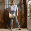Woman in a strip blouse and blue jeans stylishly posing and smiling away showing off her Dreams Blossom Hobo Bag set in a modern background.