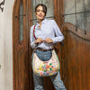 Woman in a strip blouse and blue jeans stylishly posing and showing off her Dreams Blossom Hobo Bag set in a modern background.