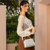 WOMEN IN A IVORY CROCKET CROP TOP AND BROWN SKIRT, LOOKING AWAY HOLDING OUR WHITE GRACIE MINI HANDBAG SET IN A MODERN BACKGROUND. 