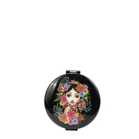ROUND COMPACT MIRROR WITH OUR  ALMA DE COLORES DESIGN. HAS A BLACK BACKGROUND , IN THE MIDDLE IS A GIRL FACE WITH BLACK HAIR LOOKING AT YOU, SURROUNDED BY COLORFULL FLOWERS AND MONARCH BUTTERFLIES.