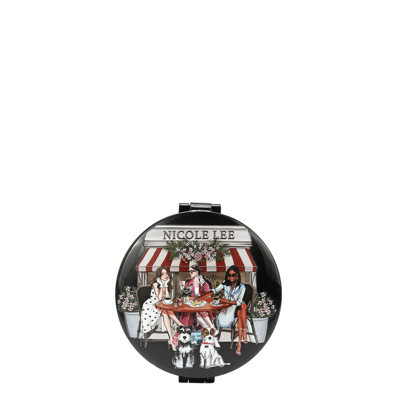 ROUND COMPACT MIRROR WITH OUR SISTERS SECRET DESIGN. THREE WOMEN SITTING IN FRONT OF A BAKERY IN A ROUND COFFEE TABLE, DRINKING COFFEE AND EATING BREAD WITH 2 SCHNAUZER DOGS UNDER THE TABLE.