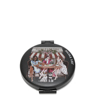 THE FRONT OF THE MIRROR HAS A BLACK BACKGROUND WITH 3 LADIES WEARING DRESSESS AND COATS. SITTING IN FRONT OF A BAKERY DRINKING COFFEE AND EATING BREAD. UNDER THE TABLE THERE'S 2 SCHNAUZER DOGS.