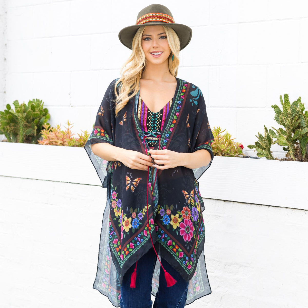 Woman in colorful top, blue jeans and boho green hat smiling wearing our Nicole Lee Kimono Alma de Colores design.