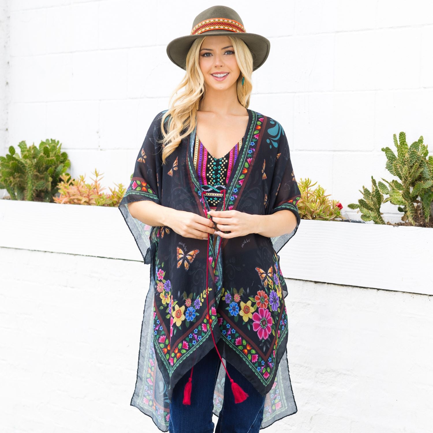 Woman in colorful top, blue jeans and boho green hat smiling wearing our Nicole Lee Kimono Alma de Colores design.