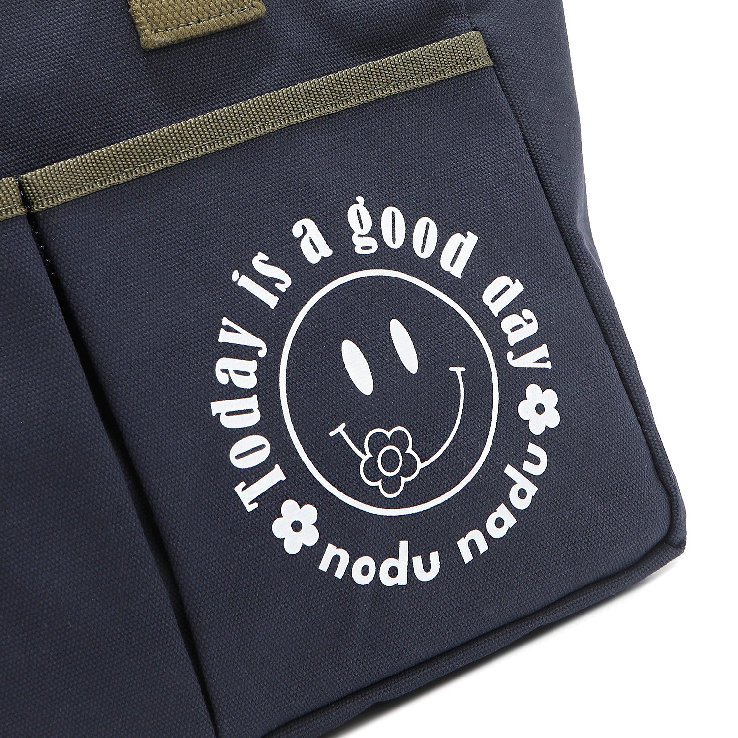 Close up detail of the Emery tote bag in navy blue with moss green trim and straps and a white "today is a good day" quote wrapped around a white smiley face with a cute little flower on its smile. Simple, minimalist, yet positive and on-trend, spread the good vibes with this classic statement. 
