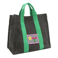Front angle view of the Nodu Nadu Sawyer Bag in Black with grass green strap accents. Charcoal black canvas adorned with a stitched logo patch in black and white checker print with nodu nadu smiley face. Front angle shows the side slip pocket to store essentials that you want close within reach like your phone, keys, wallet, lipstick, and more!