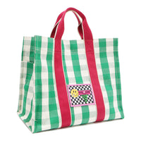 Angled front view of the Nodu Nadu Canvas Blair Bag in Green – highlighting pink handles, side panel with open slip pocket, and checkered patch. 
